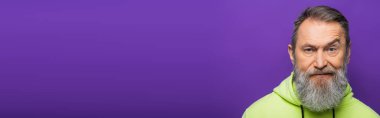 skeptical senior man moving eyebrow while looking at camera on purple background, banner clipart