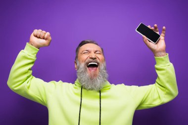 Heyecanlı, sakallı, gri saçlı, elinde mor ekranlı akıllı telefon tutan son sınıf öğrencisi. 