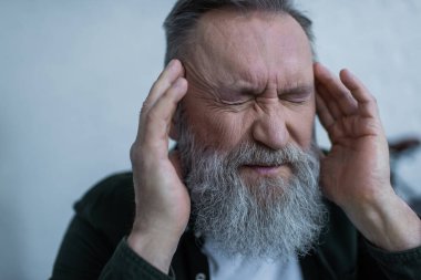 Baş ağrısı çekerken sakallı yaşlı adam kafasına dokunuyor.