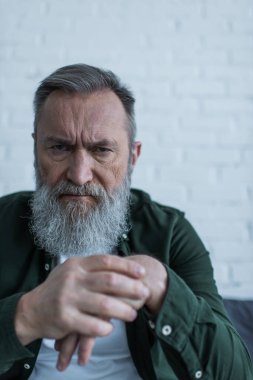 Bunalımda olan ve kameraya bakarken sakalları çatık yaşlı bir adam. 