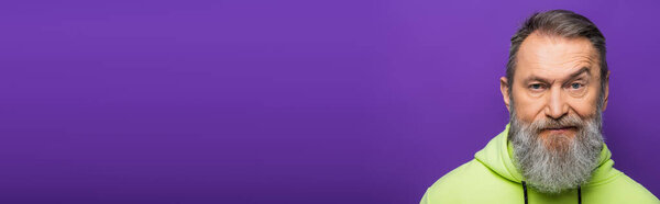 skeptical senior man moving eyebrow while looking at camera on purple background, banner