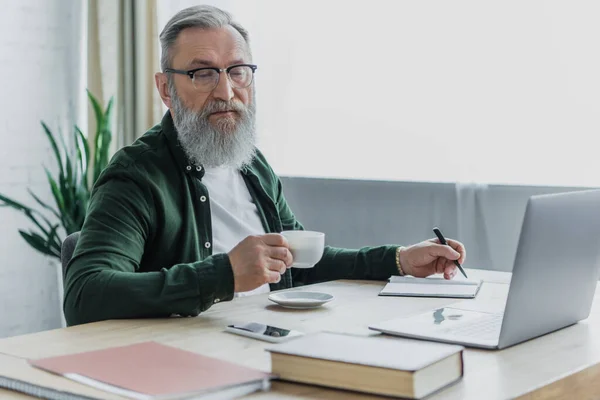 Bärtiger Älterer Mann Mit Brille Hält Tasse Kaffee Und Stift — Stockfoto