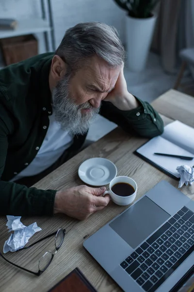 Masada Dizüstü Bilgisayara Bakarken Elinde Kahve Tutan Mutsuz Yaşlı Adamın — Stok fotoğraf