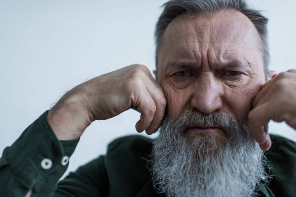 portrait of displeased senior man with beard frowning while looking at camera 