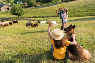 Mutlu ebeveynlere el sallayan sığır köpekli kız yeşil çayırlarda hayvan güdüyor.