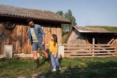 Çiftlikte yürürken el ele tutuşan baba ve kızın boyu