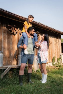 Kocasına bakan neşeli kadın ahşap ambarın yakınlarında kızını sırtında taşıyor. 