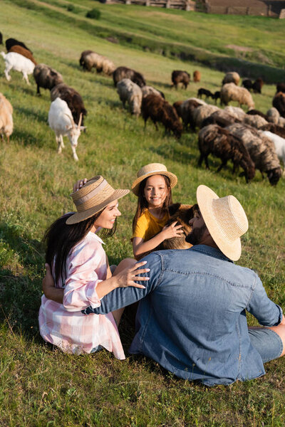 happy girl smiling near dog and parents in pasture with grazing livestock