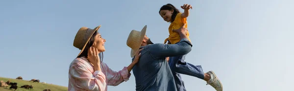 青い空バナーの下で幸せな妻の近くで娘と遊ぶ農家の低角度ビュー — ストック写真