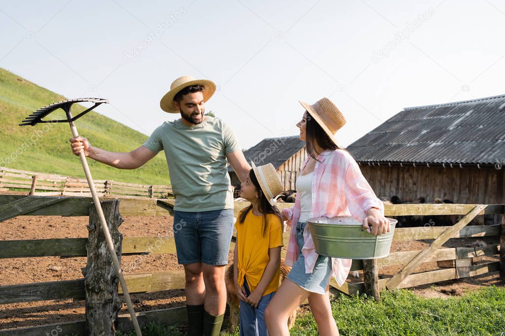 couple of farmers with rakes and bowl smiling near daughter on farm