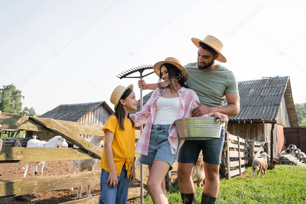 farmers with rakes and bowl smiling at daughter near corral on farm