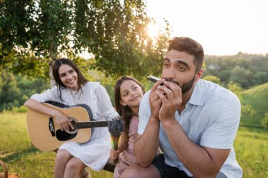 man playing harmonica near daughter with bouquet and wife with acoustic guitar clipart
