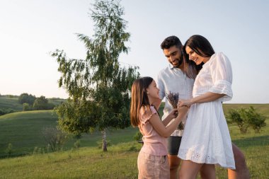 Mutlu kız ve lavanta buketi kırsal kesimde gülümseyen ebeveynlerin yanında.