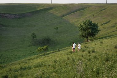 Kızıyla birlikte yaz günü dağlık çayırda yürüyen çift manzaralı.