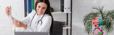 Hastanedeki bilgisayardan yapılan video aramasında, neşeli doktor belkemiği modelini tutuyor. 