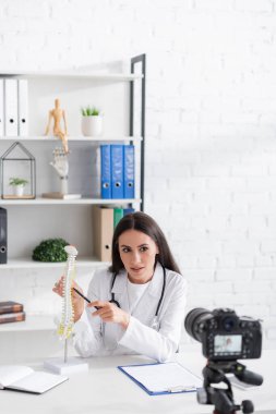 Klinikteki dijital kameranın yakınındaki omurilik modelini gösteren doktor. 