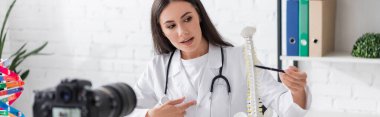 Klinikteki dijital kameranın yanında, beyaz önlüklü doktor belkemiği modelini işaret ediyor. 