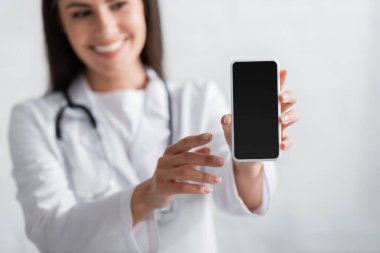 Blurred brunette doctor holding smartphone with blank screen 