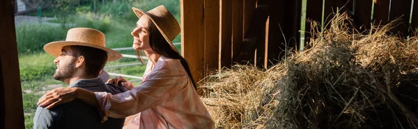 納屋の干し草の近くの夫を抱きしめる藁帽子の笑顔の女性バナー — ストック写真