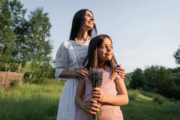 Happy Woman Hugging Shoulders Daughter Holding Lavender Flowers Outdoors — Zdjęcie stockowe