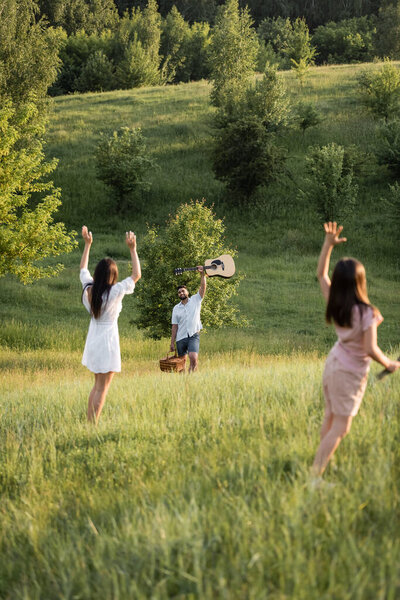 mom and daughter waving hands to man with guitar on picturesque slope