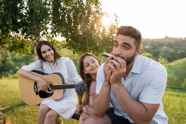 ブーケと妻と娘の近くでハーモニカを演奏する男とアコースティックギターを — ストック写真