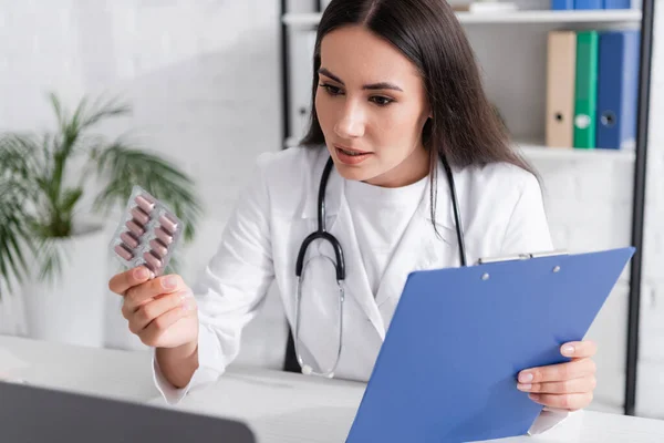 Doctor Holding Clipboard Pills Video Call Laptop Clinic — Stock Fotó