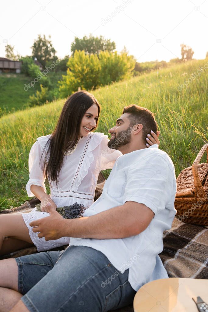 brunette woman in white dress smiling at bearded man on picnic in countryside
