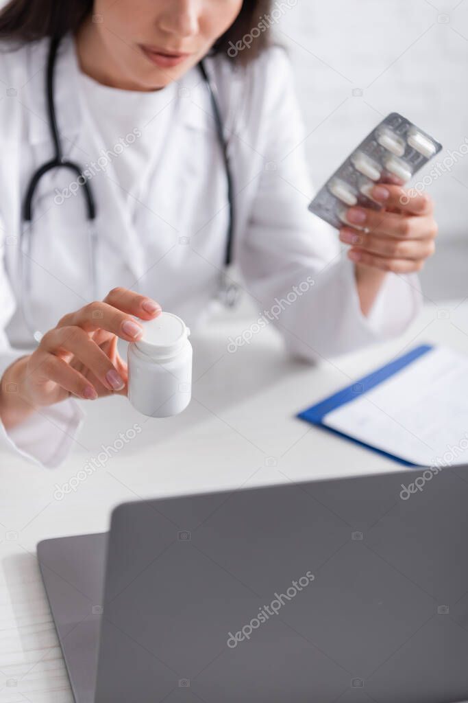 Cropped view of doctor holding pills during online consultation on laptop in hospital 