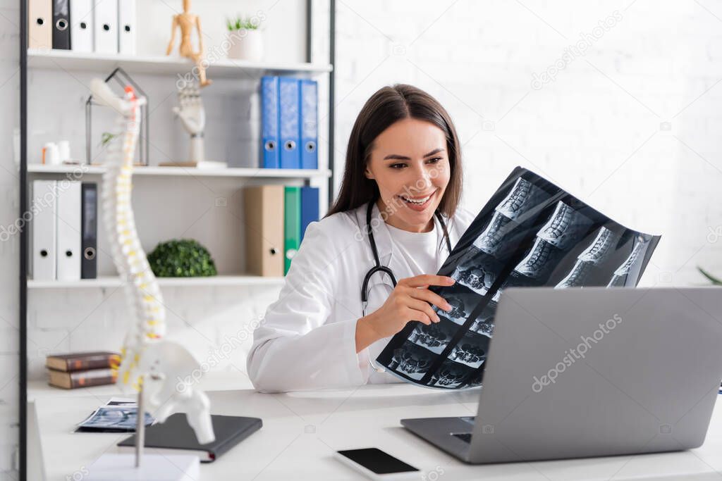 Positive doctor showing mri scan during video call on laptop in clinic 