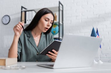 Teacher holding notebook during online lesson on laptop in class 