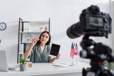 Teacher holding digital tablet and talking near laptop and camera in school 
