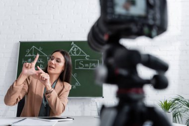 Gözlüklü öğretmen matematik formülleri ve sınıfta bulanık dijital kamerayla karatahtanın yanında el kol hareketi yapıyor. 