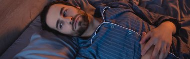 Young man suffering from insomnia on bed, banner 