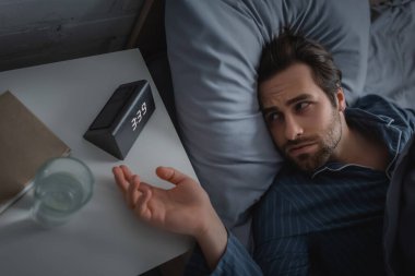 Uykusuzluk çeken bir adamın komodindeki elektronik çalar saate bakışı. 