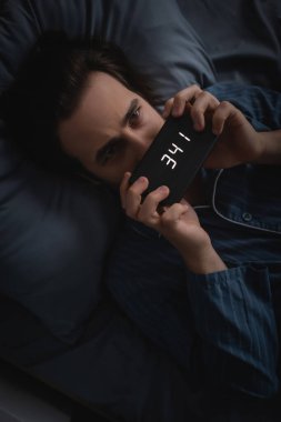 Top view of man holding electronic clock on bed at night 