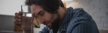 Sabah uykusuzluk çekerken elinde bir bardak su tutan genç adam, afiş. 