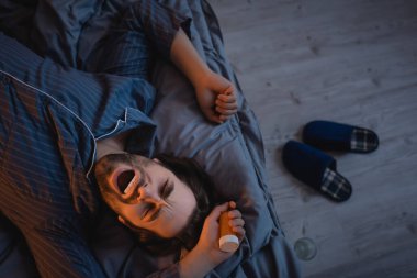 Top view of man with insomnia holding pills and yawning on bed 