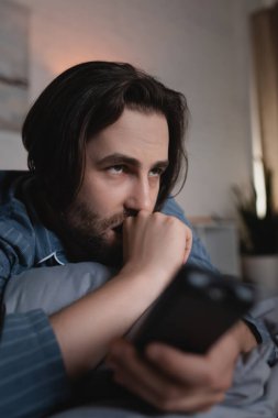 Geceleri uykusuzluk çeken stresli bir adam bulanık uzaktan kumandayı yatakta tutuyor. 