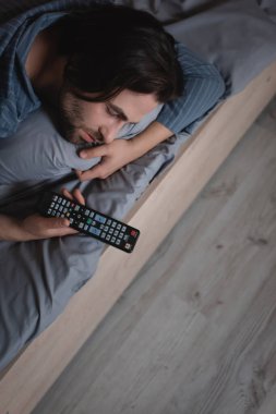 Geceleri yatakta uyurken uzaktan kumanda tutan adamın yüksek açılı görüntüsü 