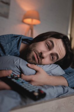 Man with insomnia holding blurred remote controller on bed 