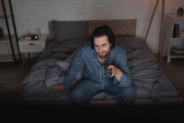 Displeased man with insomnia watching movie in bedroom at night 