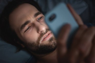 Yorgun bir adamın gece yatakta akıllı telefon kullanmasının en üst görüntüsü. 