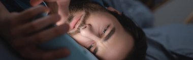 Young man suffering from sleepless and using smartphone in bedroom, banner  