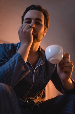 Uykusuzluk çeken ve elinde bir fincan kahve tutan üzgün adamın düşük açılı görüntüsü. 