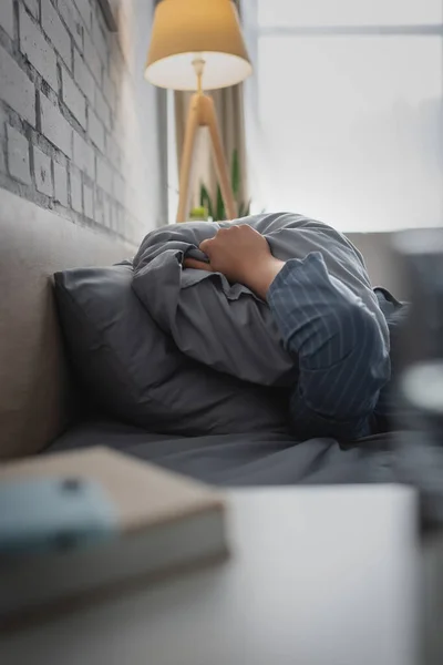 早上穿着睡衣 头戴枕头的男人躺在床上 — 图库照片