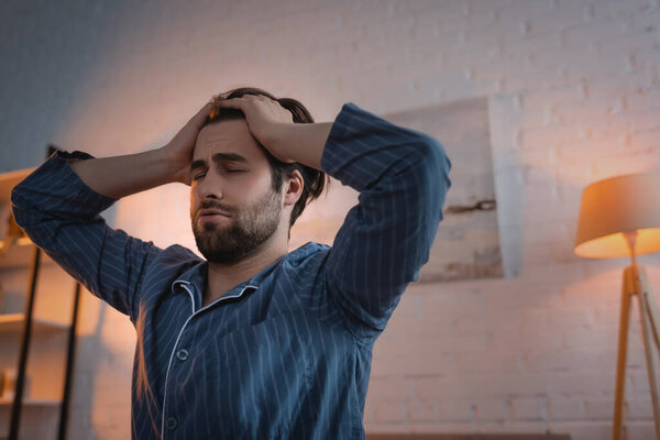 Exhausted man in pajama touching head in bedroom at night 