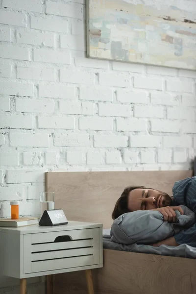Young Man Closed Eyes Lying Pillow Pills Alarm Clock Bedroom — Stockfoto