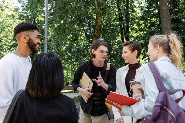 Students with backpacks talking near multicultural friends in park 