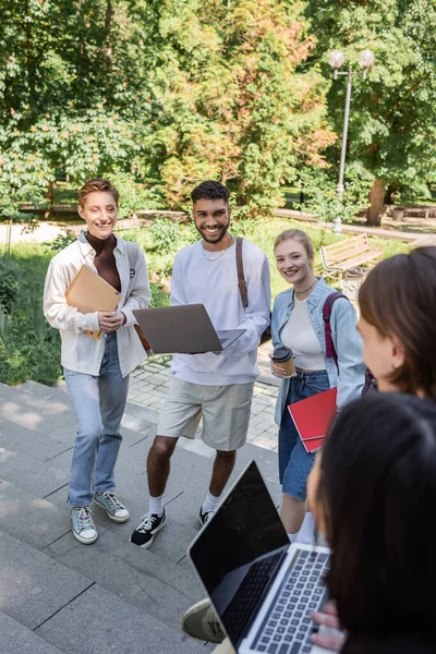 带着笔记本电脑和咖啡的快乐的多种族学生去公园看模糊的朋友 — 图库照片
